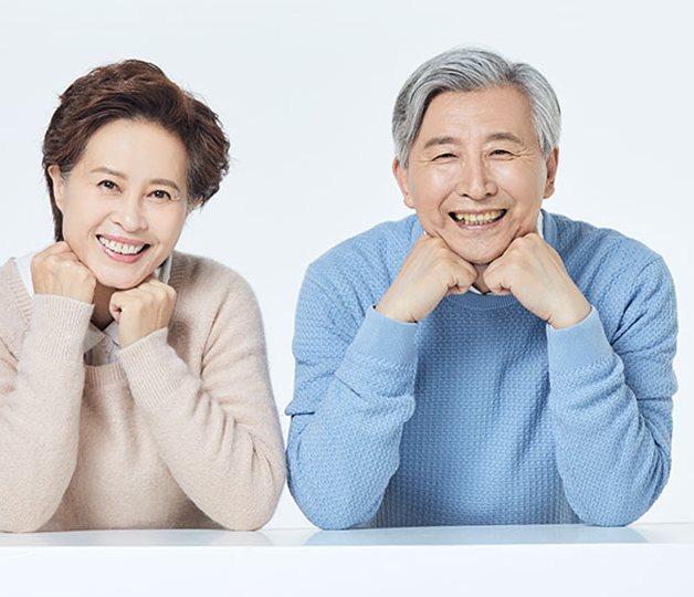 연하늘 바탕, 흰 탁자에 턱을 괴고 웃는 노년 부부(광고 모델)
